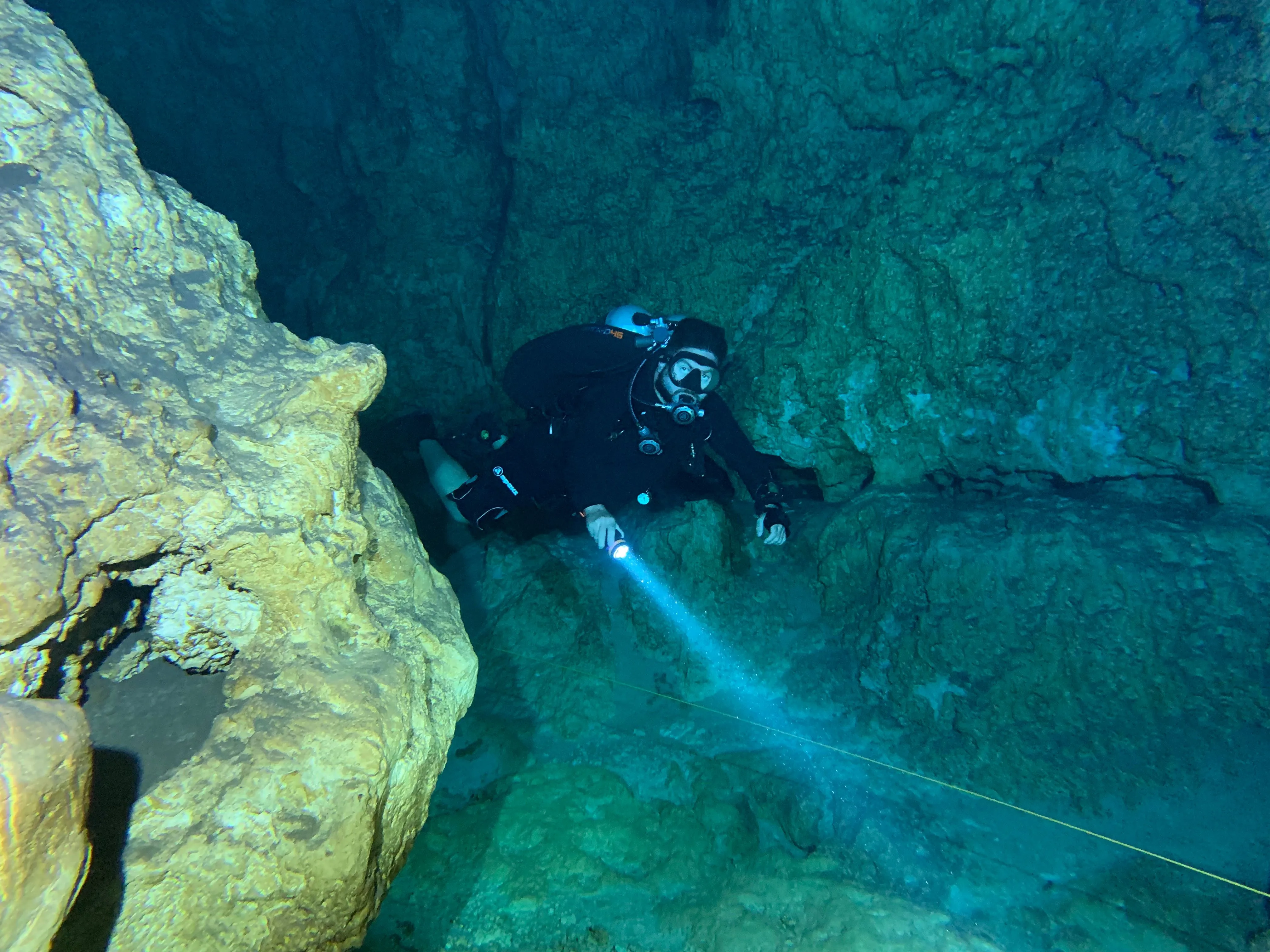 A diver with a flashlight follows a guideline through an underwater cave
