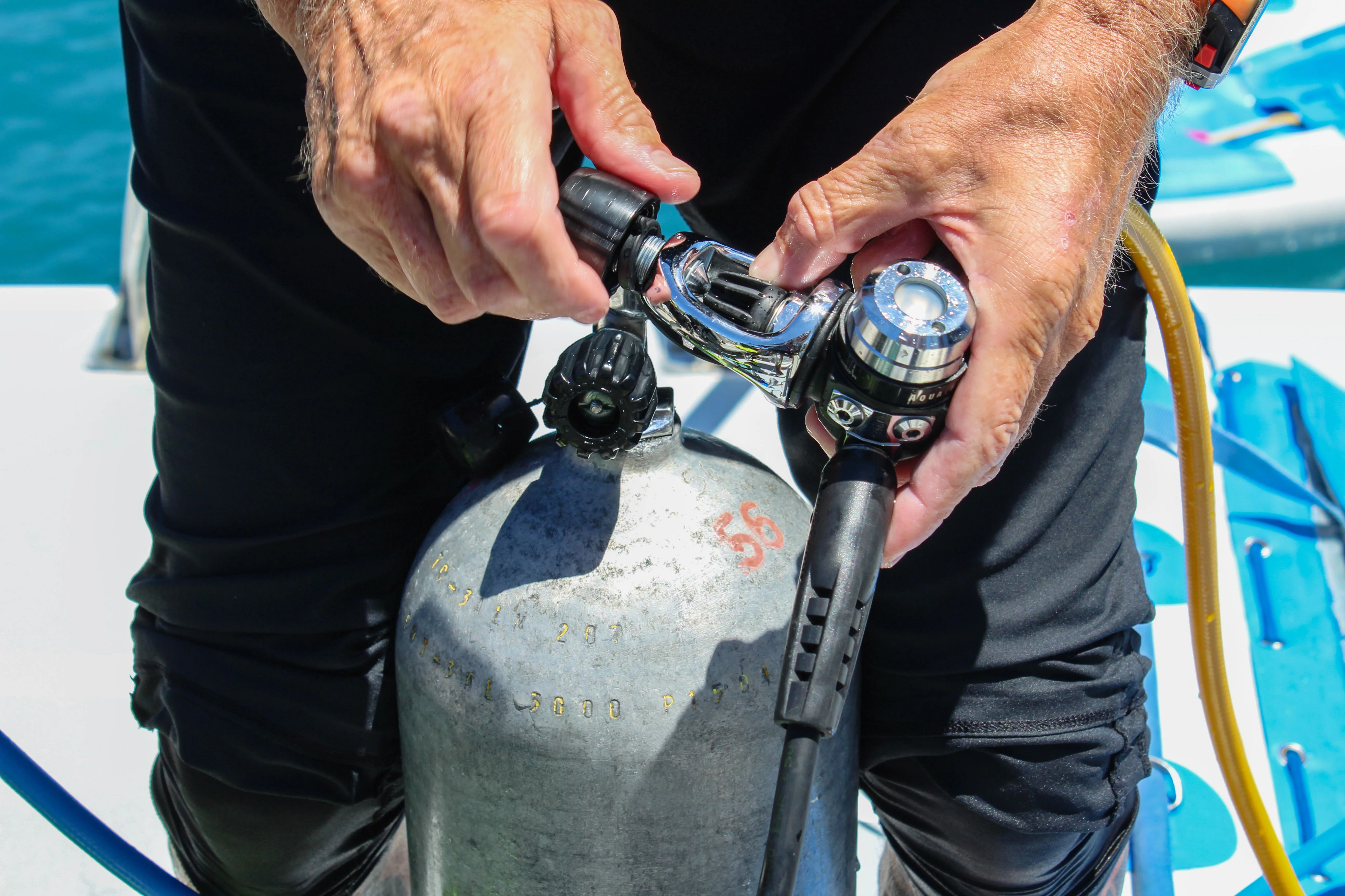 A diver connects a regulator to a scuba cylinder aboard a boat