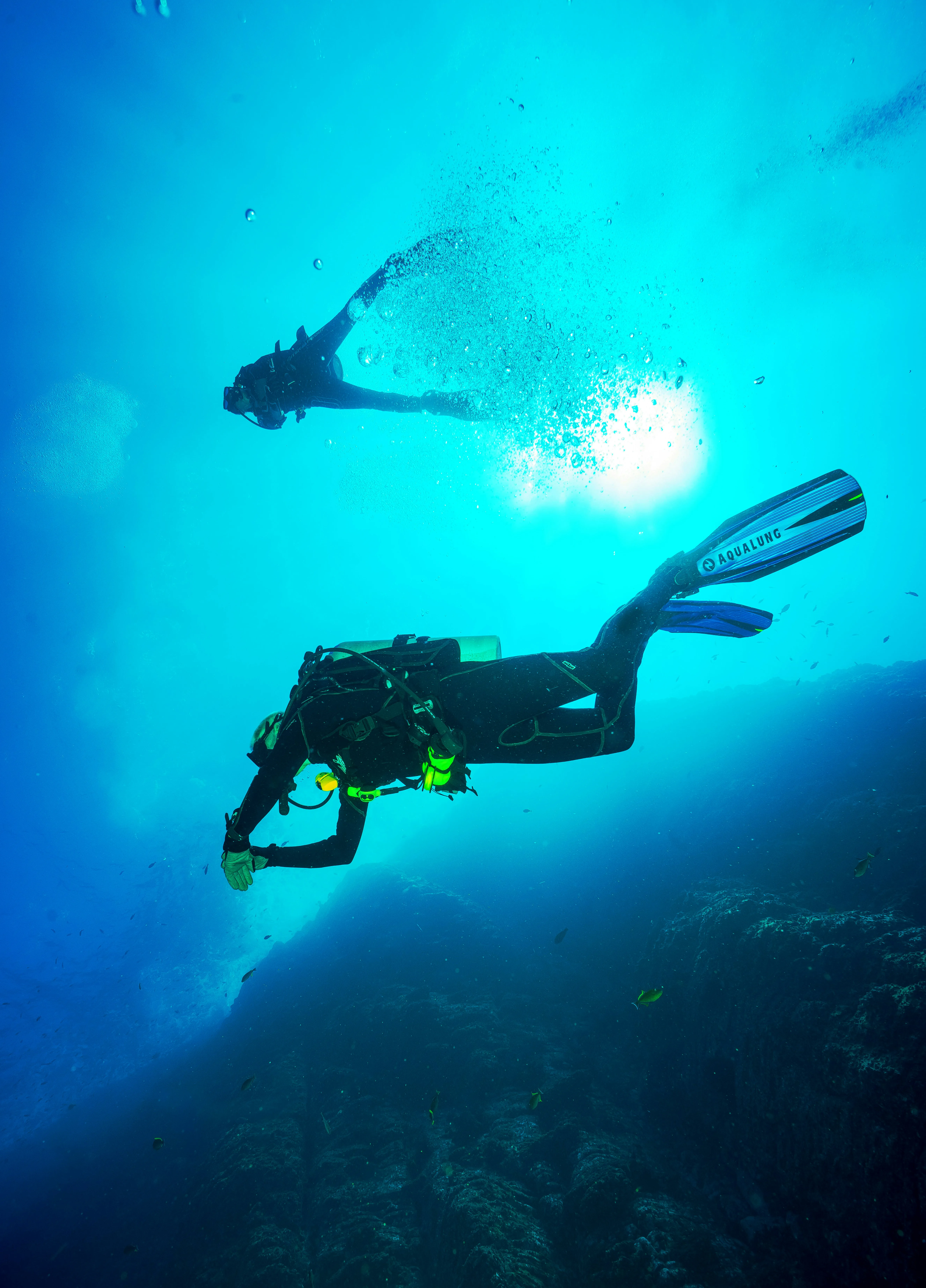 Two scuba divers swim at different depths in clear blue water